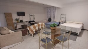 Un espacio habitable compacto con sofá, una mesa de comedor con sillas, cama, televisor y una mesita auxiliar.