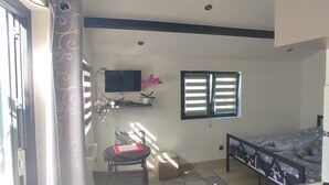 Una cocina compacta con un lavamanos, una zona de comedor con una silla y una mesa, un televisor montado en la pared y una ventana con persianas.