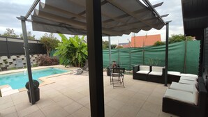 Un espacio al aire libre techado con piscina, sillas de descanso y una mesa.
