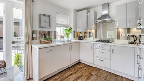Une cuisine moderne avec des meubles blancs, un plancher en bois et un coin repas doté d’une table en verre.