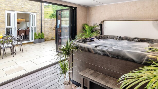 Un espace patio extérieur moderne comprenant un jacuzzi, une table à manger avec des chaises et une porte vitrée donnant sur un jardin.