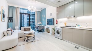 Eine moderne Wohnung mit Wohnzimmer, Essbereich und Küche. Sie verfügt über ein großes Fenster, eine Chandelierleuchtre und eine Waschmaschine.