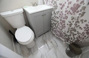 Bathroom features a toilet, sink, and shower area with storage.
