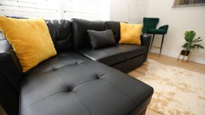 A black leather sectional sofa with two yellow cushions, a green chair, and a small plant.