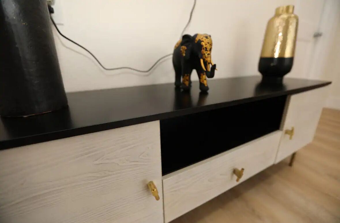 A black and white cabinet with gold handles, a black object on the left, and a golden vase on the right.
