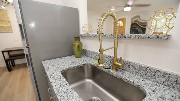 A kitchen with a stainless steel sink, granite countertop, and a gold faucet.