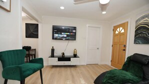 A living room with a flat-screen TV mounted on the wall, a wooden door, and a green armchair.