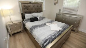 A bedroom with a bed, nightstands, a dresser, and a window with blinds.