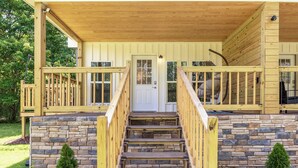 A wooden cabin with a stone foundation, a front porch with a staircase, and a door.