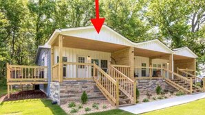 A two-story house with a porch, wooden stairs, and a stone foundation.