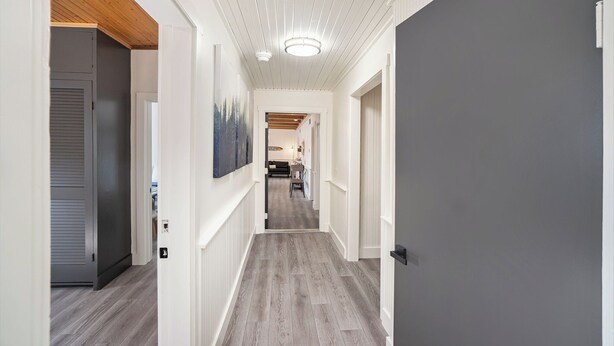 A hallway with wooden flooring, white walls, and a ceiling with wooden beams.