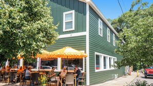 A green building with a row of outdoor tables and chairs under a yellow umbrella, suggesting a cafe or restaurant setting. - Spacious downtown apartment with parking (Douglas)