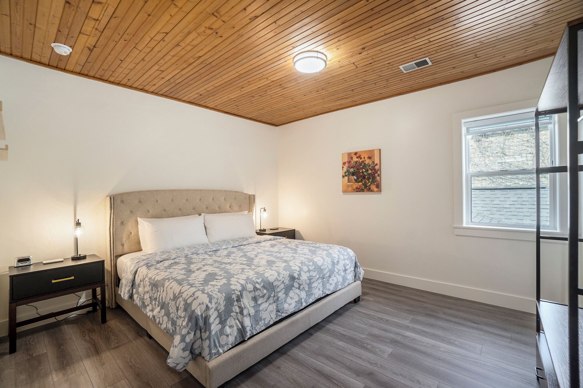 Ein Schlafzimmer mit Bett, Nachttischen, Fenster und Holzboden.