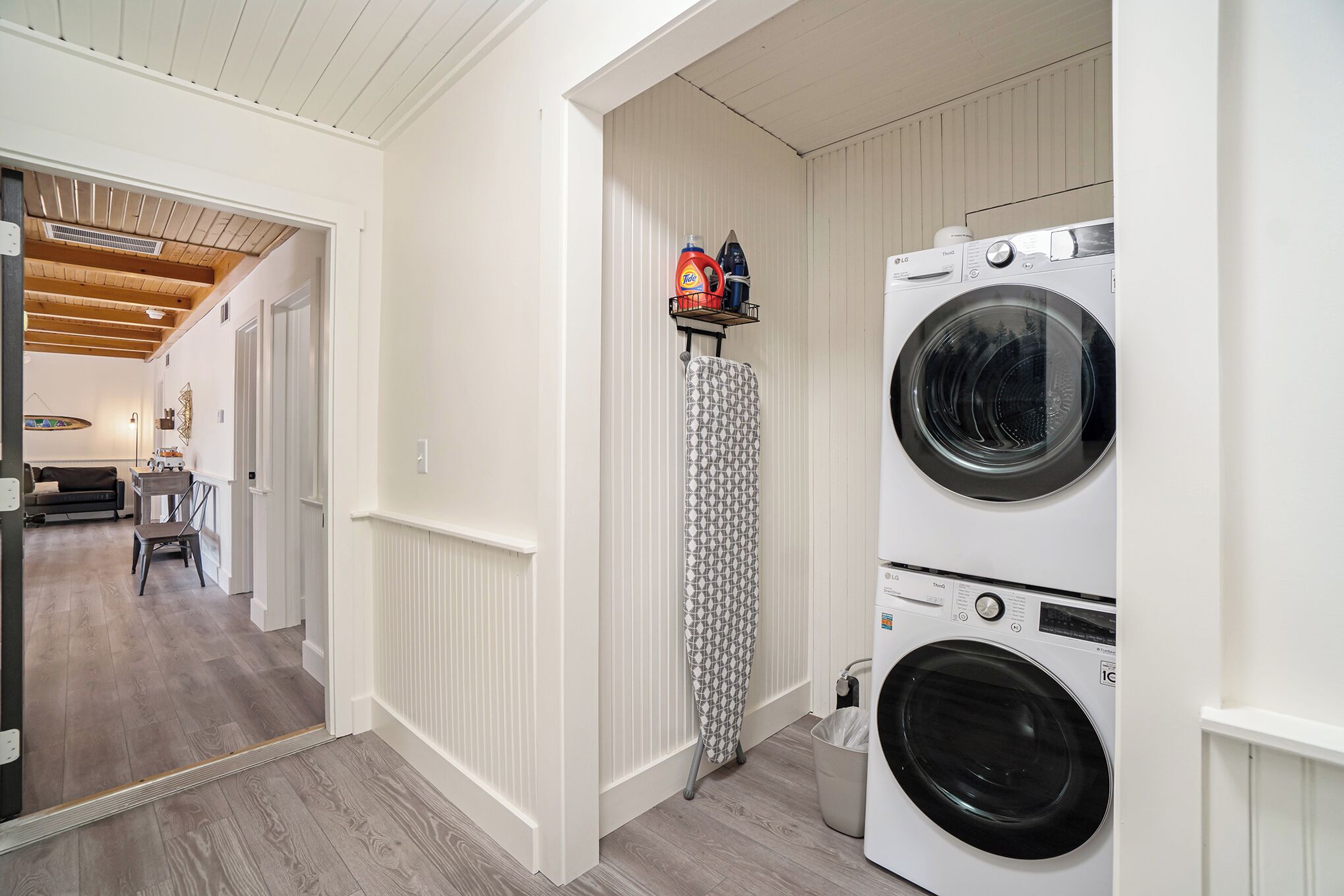A laundry room with two stacked front-loading washing machines, a drying rack, and a shelf with laundry supplies.
