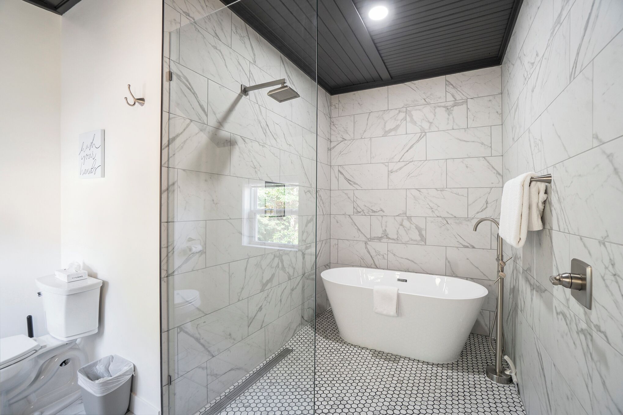 Un baño moderno con una bañera independiente, ducha con mampara de cristal y suelo de mármol.