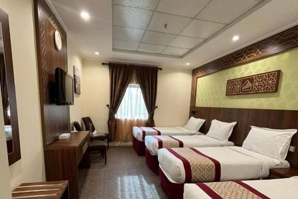A hotel room with four beds, a desk, a TV, and a clock on the wall.