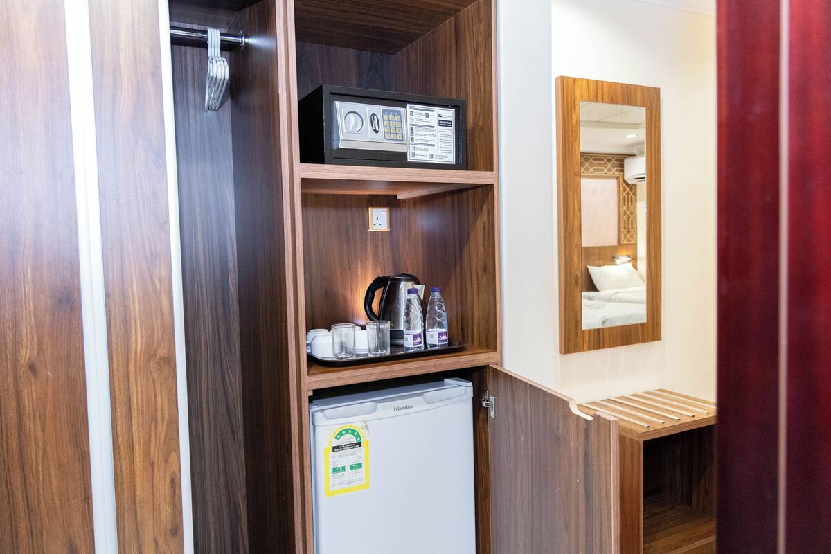 A compact hotel room with a wooden wardrobe, a small refrigerator, a microwave, and a mirror.