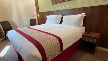 A hotel room with a large bed, a wooden headboard, a nightstand, and a wall with a geometric pattern.
