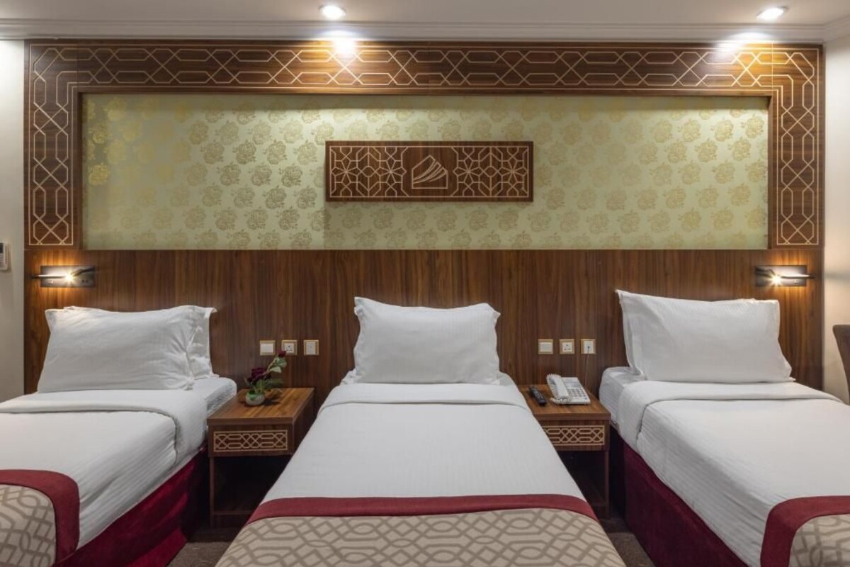 Habitación de hotel con dos camas, cabecero de madera, papel tapiz estampado y lámparas de noche.