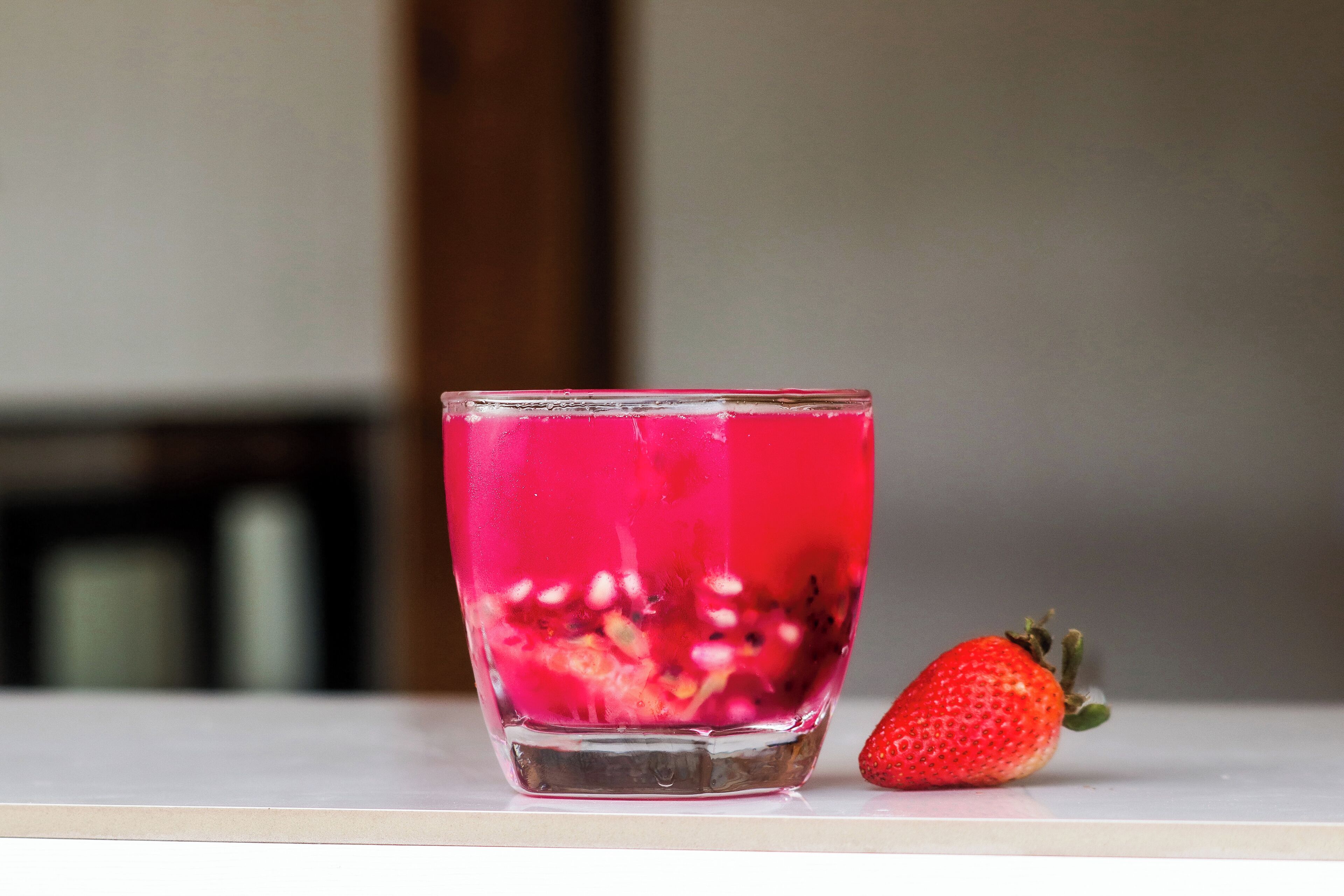 A glass of pink beverage with a strawberry beside it.