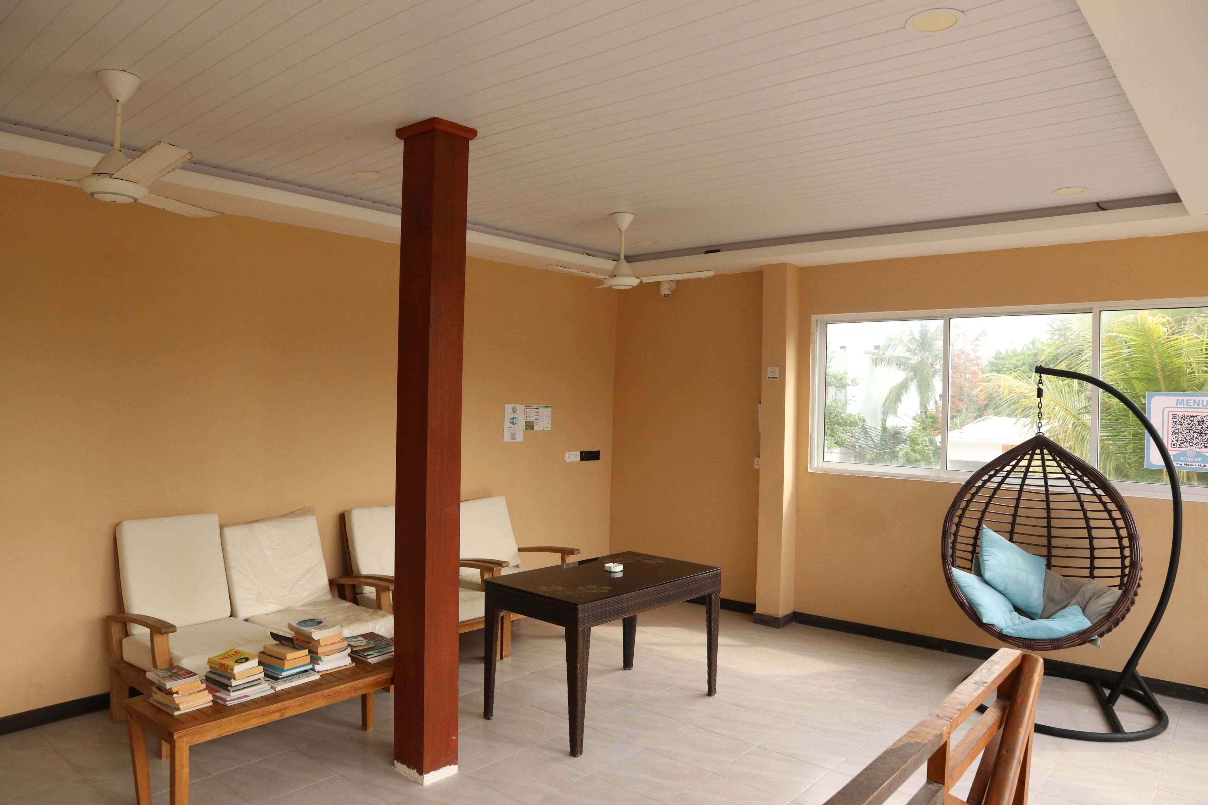 A room with a sofa, a wooden table, a hanging chair, and a window with a view of palm trees.