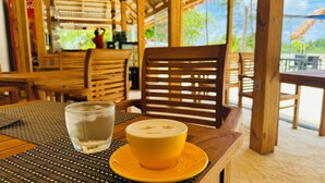 Une table avec un verre d’eau et une tasse de café, des chaises en bois et une vue sur la verdure à l’extérieur.