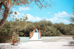 A wooden pier leading to a gazebo over a beach with clear turquoise water.