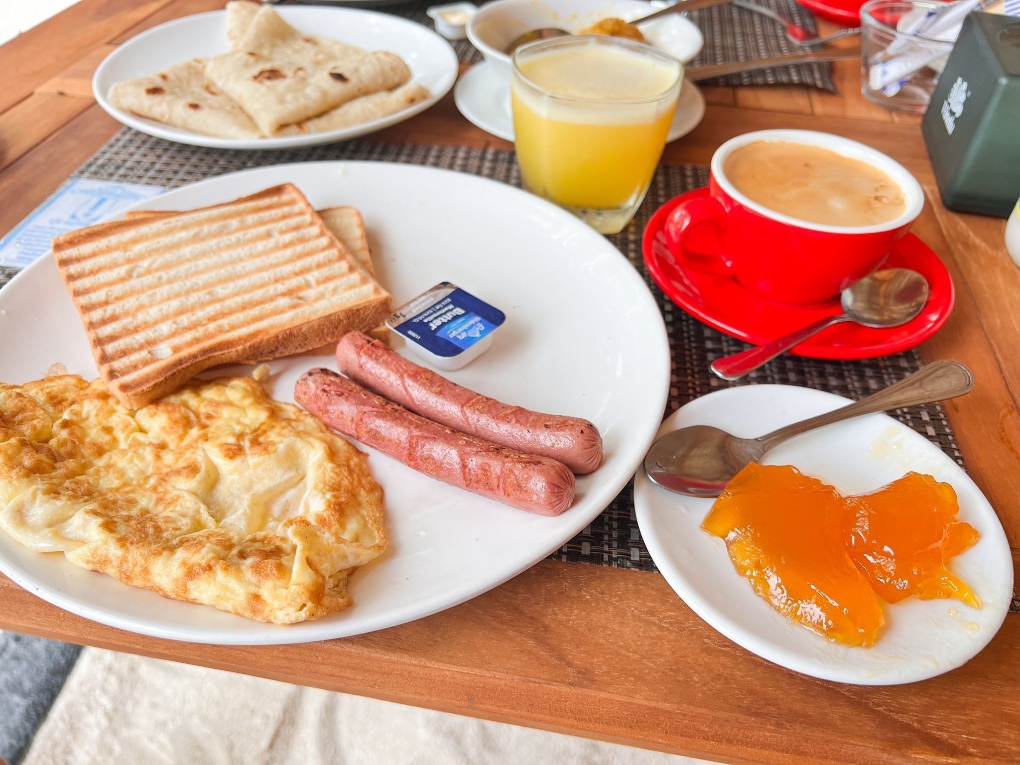 A breakfast plate with toast, sausages, scrambled eggs, and orange jam.