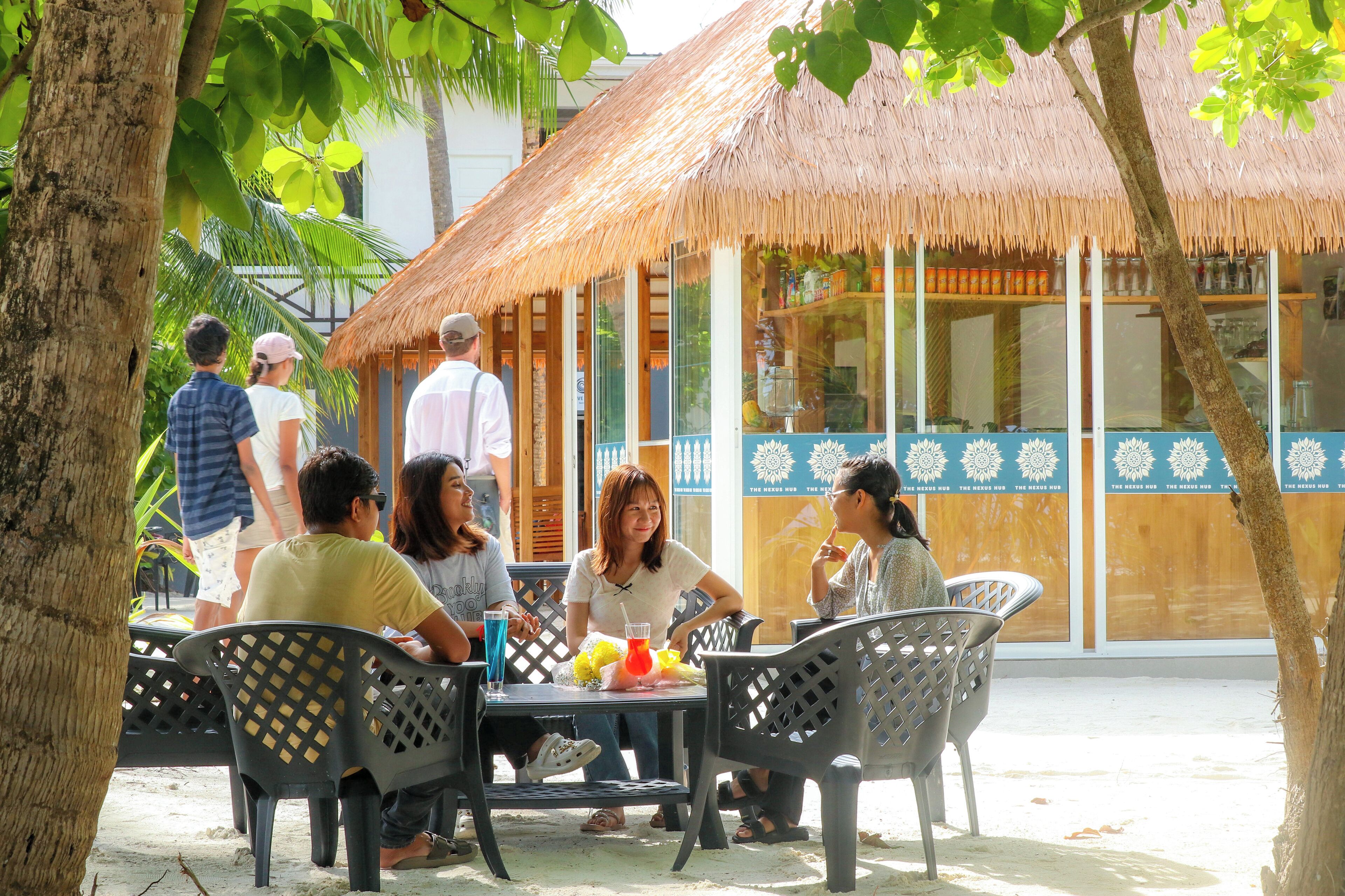 A group of people seated at an outdoor table with a thatched roof structure in the background.