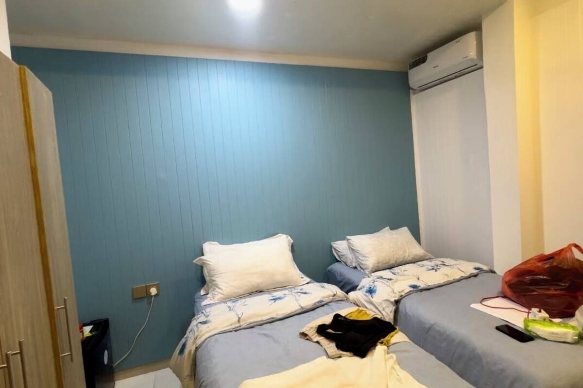 A bedroom with two beds, a wooden wardrobe, and an air conditioning unit.