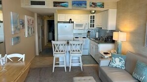 A compact living space with a kitchenette, a dining area, and a seating area with a sofa and ottoman.