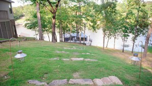 Une zone herbeuse avec des marches en pierre menant à un quai au bord d’un lac, le tout entouré d’arbres et d’un bâtiment.