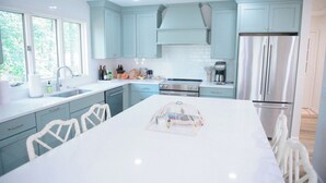 Une cuisine moderne avec des meubles bleu clair, un grand îlot central, des appareils en acier inoxydable et une vue sur la verdure à l’extérieur.