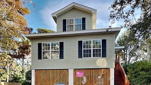 A two-story building with a garage, a wooden fence, and a staircase leading to the upper level. - Spacious, Marsh View Getaway w/ Multiple Outdoor Decks (Tybee Island)