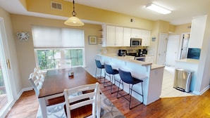 A compact kitchen with white cabinets, a central island with bar stools, and a dining table with chairs. - Spacious, Marsh View Getaway w/ Multiple Outdoor Decks (Tybee Island)