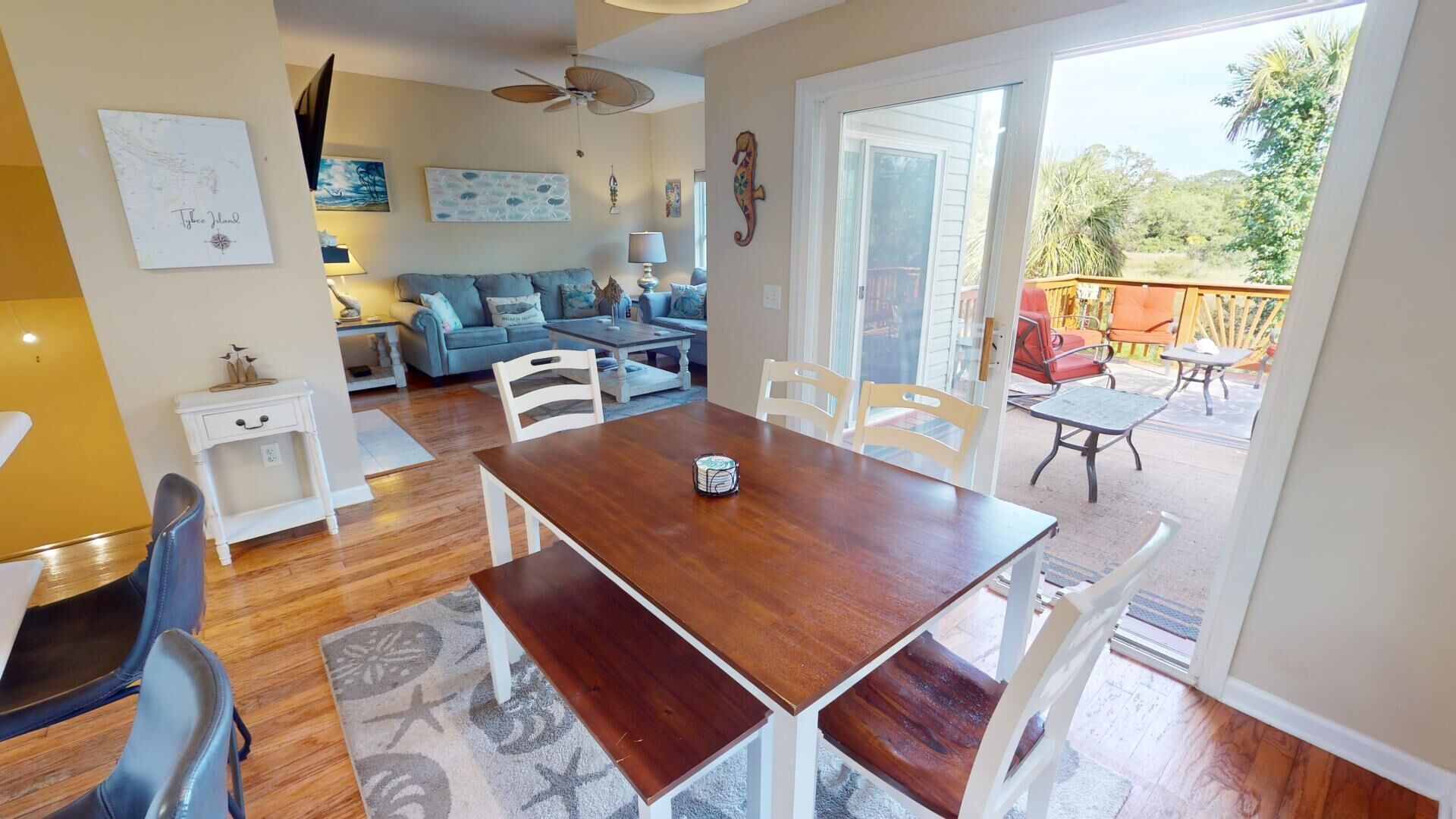 A spacious living area with a wooden dining table, white chairs, a sofa, and a balcony with outdoor seating.
