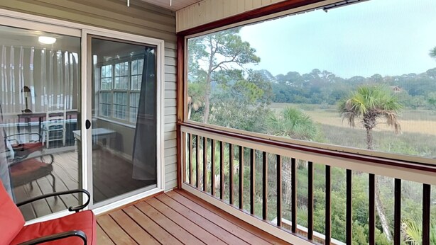 A wooden deck with a glass door leading to a room with a desk and chair. - Spacious, Marsh View Getaway w/ Multiple Outdoor Decks (Tybee Island)