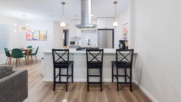 A modern kitchen with a central island, bar stools, and pendant lighting. - 2BR Ensuite | Near UT & The Domain (Austin)