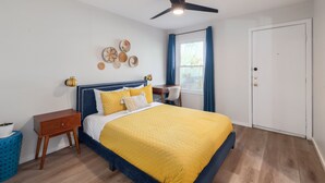 A bedroom with a bed, a ceiling fan, a desk, a chair, a window with curtains, and a door. - 2BR Ensuite | Near UT & The Domain (Austin)
