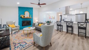 A modern living room with a fireplace, a dining area with bar stools, and a kitchen with a stainless steel refrigerator. - 2BR Ensuite | Near UT & The Domain (Austin)
