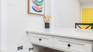 A kitchen with white cabinets, a yellow door, and a colorful abstract painting. - 2BR Ensuite | Near UT & The Domain (Austin)