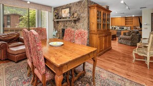 A spacious living area with a wooden dining table, floral upholstered chairs, a stone accent wall, and a view of a brick building through large windows. - Spacious 4 bedroom condo in the heart of Vail Village, great value!! (Vail)
