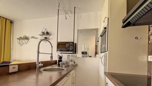 Eine kompakte Küche mit Spüle, Mikrowelle und Herd. Über dem Herd befindet sich ein Spiegel und eine kleine Ablage mit Dekoration.