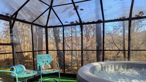 Un bain à remous situé dans un espace extérieur abrité, avec des chaises et une table, le tout entouré d’arbres.