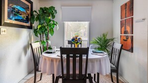 A dining area with a round table, two chairs, a potted plant, a window with blinds, and framed artwork on the walls. - Zilker Park, Town lake, and Barton Springs pool (Austin)