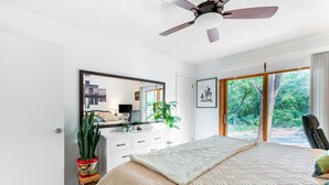 A bedroom with a bed, a ceiling fan, a dresser, a mirror, a window with a view of trees, and a potted plant. - Zilker Park, Town lake, and Barton Springs pool (Austin)