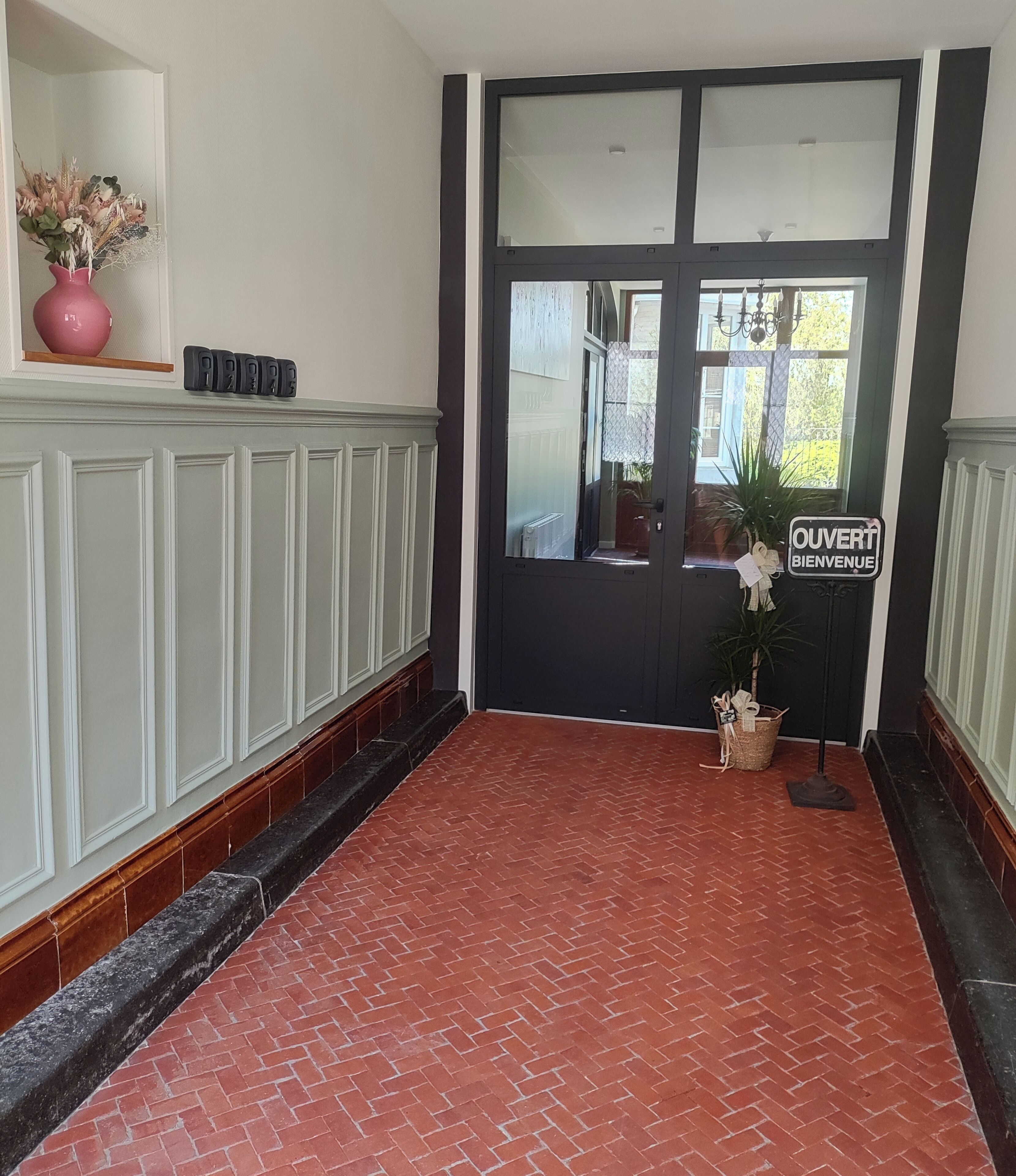 A hallway with a red brick floor, a black door with a glass panel, and a welcome sign.