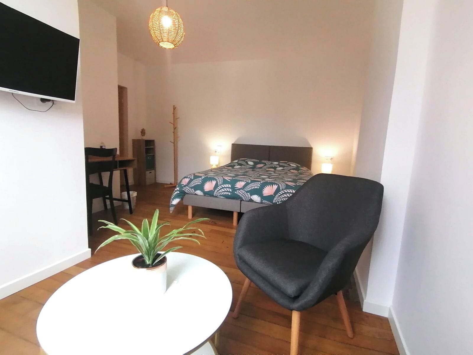 Una habitación pequeña y bien iluminada con una cama, un escritorio, una silla y una planta en maceta.