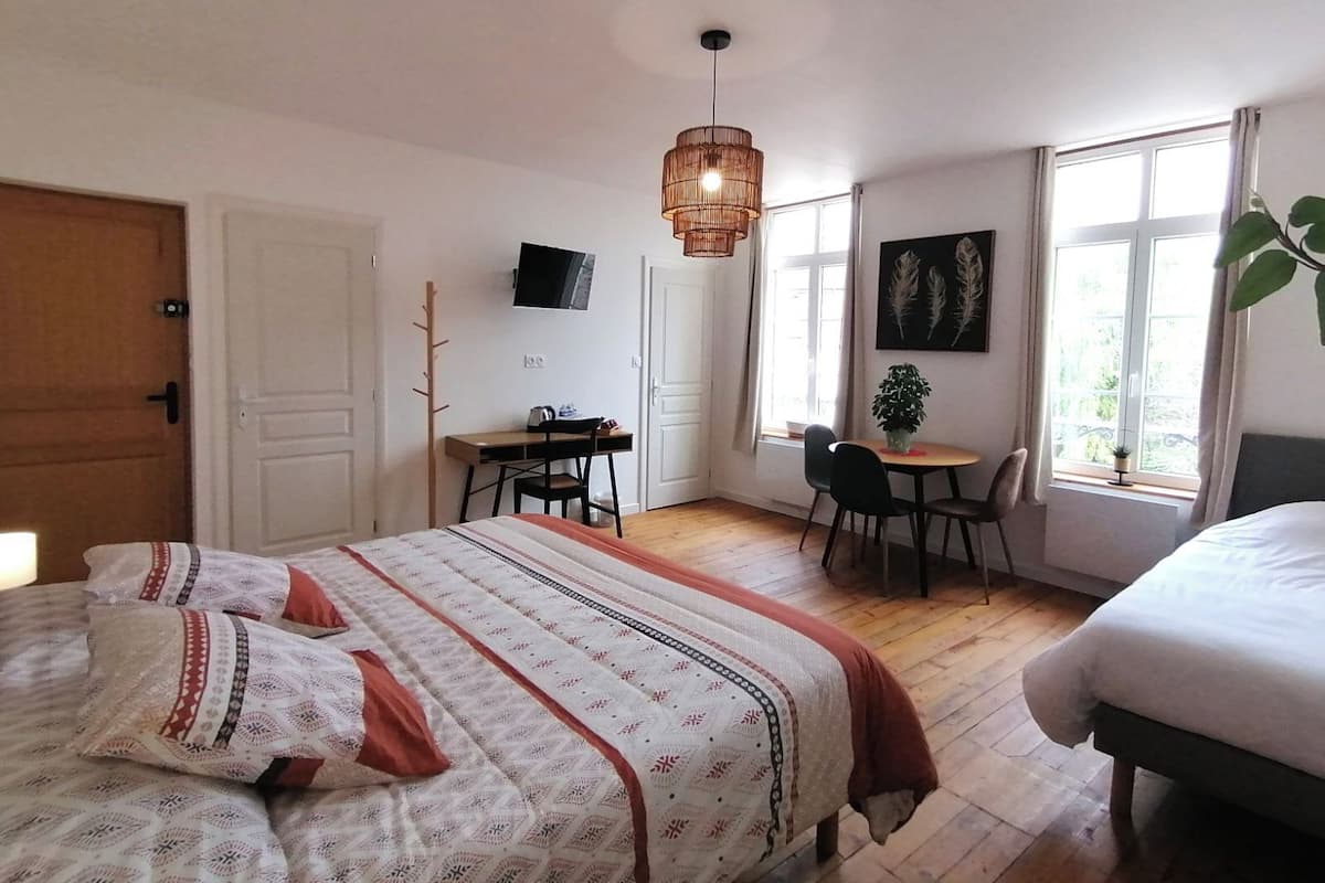A bedroom with a bed, a desk, a chair, a TV, and a window with curtains.