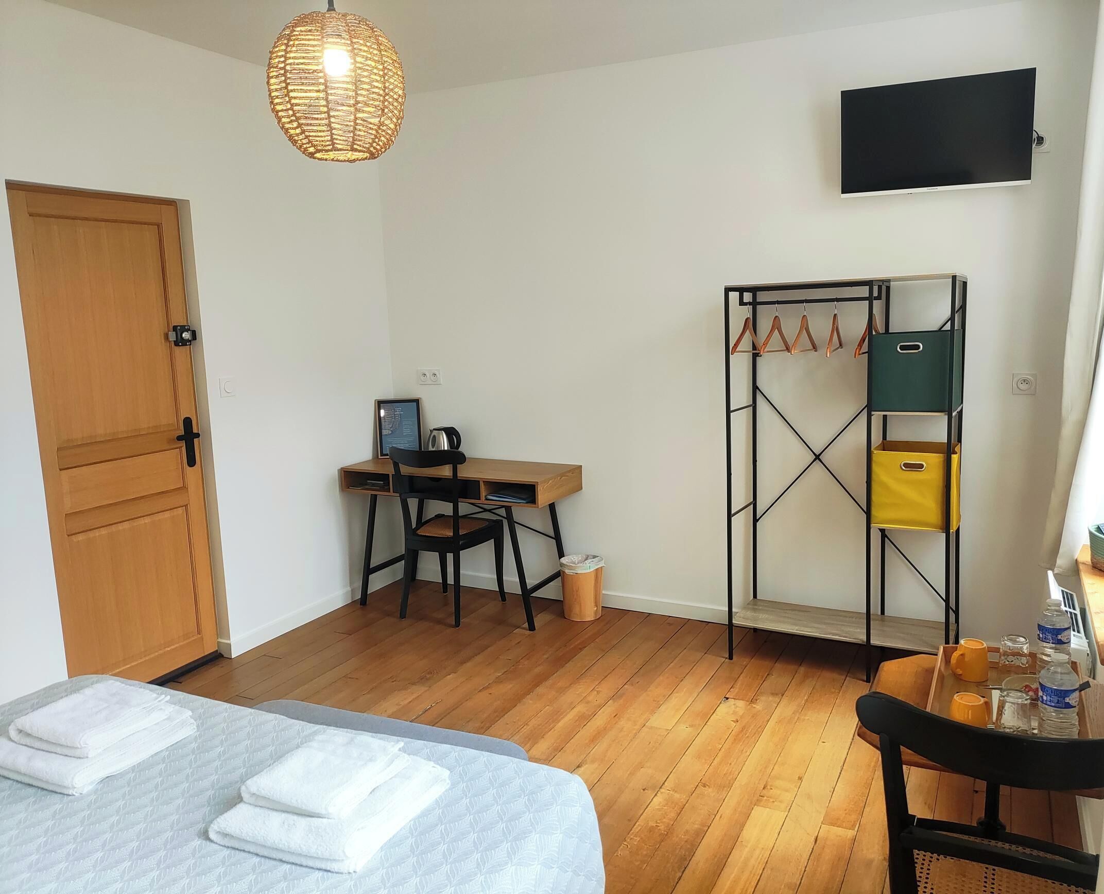 Una habitación con cama, escritorio, silla, televisión y perchero.